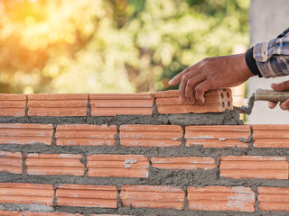 worker placing bricks on cement while building exterior walls in construction site