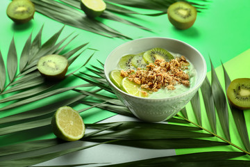 Tasty granola with yogurt and fruits in bowl on color background
