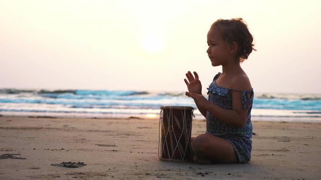 Cute little child girl playing drums on sandy beach. 
