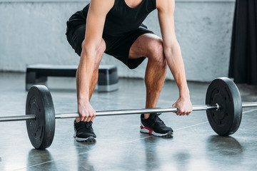 Fototapeta na wymiar cropped shot of muscular young man in sportswear lifting barbell in gym