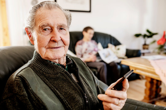 Senior sitzt zuhause im Wohnzimmer und surft auf seinem smart phone im Internet
