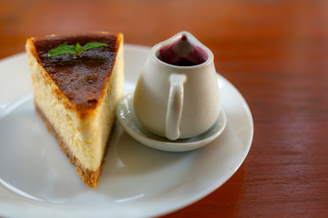 Slice of gourmet fresh cake pie with a jar of blueberry on a white plate with wooden table background.