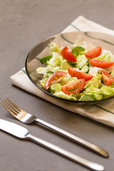 healthy salad, vegetable, tomatoes, cucumbers, iceberg, Cutlery, kitchen towel, grey background. Copy space. Vegetarian