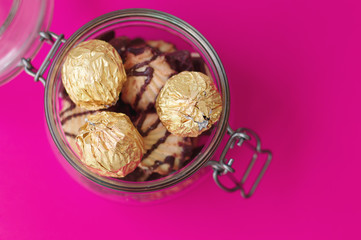 Jar with sweets and cookies on pink background. Sweets in golden foil and biscuits, top view