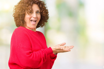 Beautiful middle ager senior woman red winter sweater over isolated background Pointing to the side with hand and open palm, presenting ad smiling happy and confident