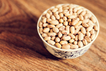 Beans (Phaseolus) in white porcelain bowl on wooden background, vegetarian concept.