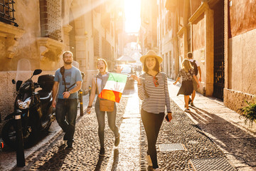 Three young friends tourists walking down the city street with italian flag