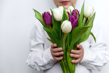 Child holding bouquet of white and purple tulips in hands. Valentines day, mothers day or birthday celebration concept. Selective focus. Copy space