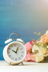 White alarm clock and flowers pink and red rose on wooden table and blue background with copy space for add text and content.