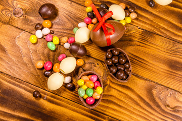 Chocolate easter eggs and multicolored candies on wooden table. Top view