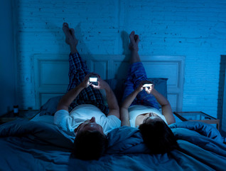 Couple on mobile phones in bed late at night enjoying social network, games and internet connection