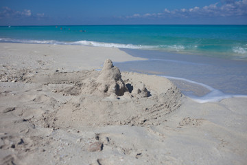 Sand castle on the beach. Fragile sand house near the sea wave