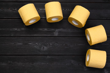 Yellow toilet paper on black wooden background top view