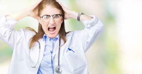 Middle age mature doctor woman wearing medical coat over isolated background Crazy and scared with hands on head, afraid and surprised of shock with open mouth