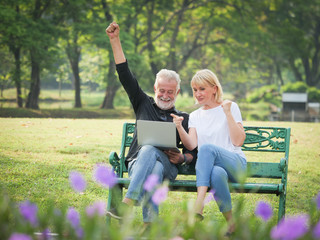 Two happy seniors retirement Man and woman are sitting and using computer laptop in park