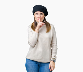 Middle age mature woman wearing winter sweater and beret over isolated background asking to be quiet with finger on lips. Silence and secret concept.