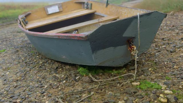 Rustic wooden rowboat dinghy beached on rocky shore. Camera tilts up.