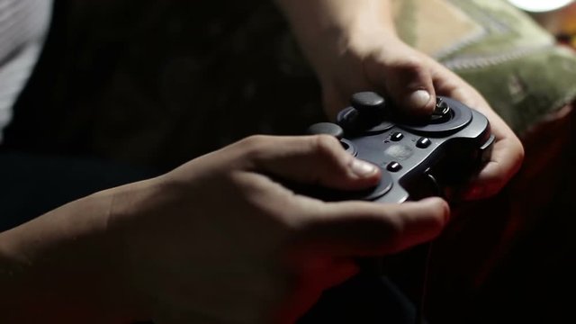 Gamer holding a joystick in his hands and playing video games, close-up