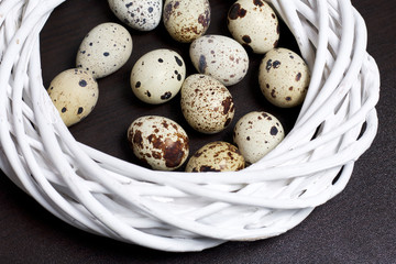 Quail eggs. Lie on paper shavings. In a wreath of wicker vines. On a dark background.