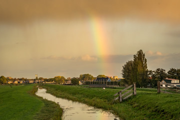 Typical dutch landscape with rainbow in the western part of Holland. Scenic view of a rainshower with bright rainbow in the dutch countryside.