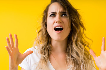 Young beautiful blonde woman over yellow background crazy and mad shouting and yelling with aggressive expression and arms raised. Frustration concept.