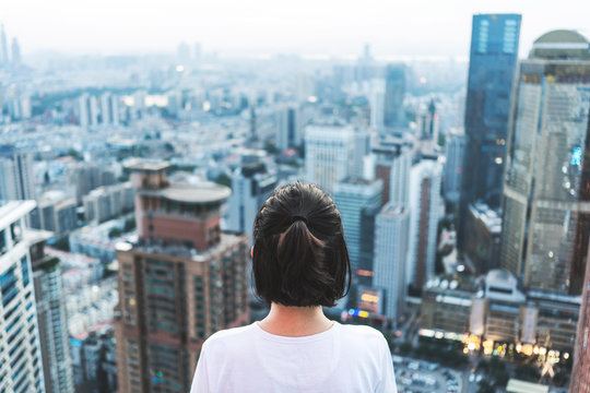 Young woman looks out over the city at the top of the building
