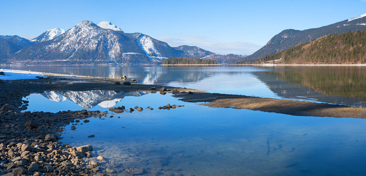 Seeufer Walchensee am Ende des Winters mit Spiegelung der Berge im Wasser