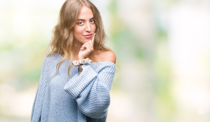 Beautiful young blonde woman wearing winter sweater over isolated background looking confident at the camera with smile with crossed arms and hand raised on chin. Thinking positive.