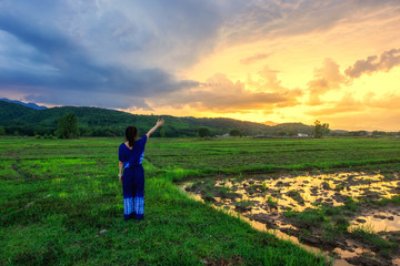 Young woman is looking green field with mountains at sunset.