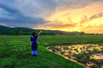 Fototapeta premium Young woman is looking green field with mountains at sunset.