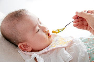 Asian Mother feeding daughter baby food