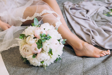 feet of the bride next to the wedding bouquet on the bed