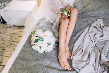 Obraz na płótnie Canvas feet of the bride next to the wedding bouquet on the bed