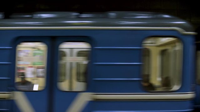 Blue subway train with people inside picking up speed, view from metro station. Close up for windows of subway train passing fast at underground station.