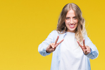 Fototapeta premium Beautiful young blonde woman over isolated background smiling looking to the camera showing fingers doing victory sign. Number two.