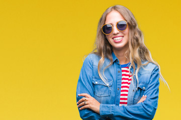 Beautiful young blonde woman wearing sunglasses over isolated background happy face smiling with crossed arms looking at the camera. Positive person.