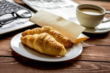 Business lunch with croissant and laptop on wooden desk