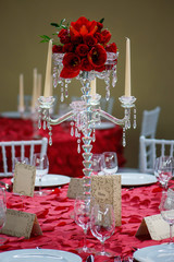 Vertical perspective of a romantic formal table, a beautiful crystal candelabra style candle holder centerpiece with eight scalloped bobeche for candlesticks and a red tulips and roses bouquet