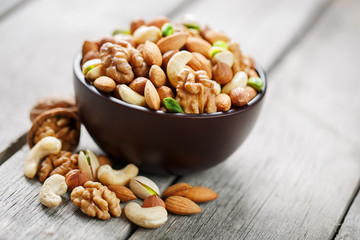 Wooden bowl with mixed nuts on a wooden gray background. Walnut, pistachios, almonds, hazelnuts and cashews, walnut.