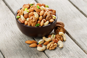 Wooden bowl with mixed nuts on a wooden gray background. Walnut, pistachios, almonds, hazelnuts and cashews, walnut.