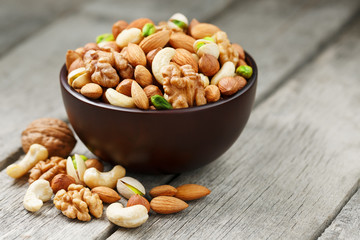 Wooden bowl with mixed nuts on a wooden gray background. Walnut, pistachios, almonds, hazelnuts and cashews, walnut.