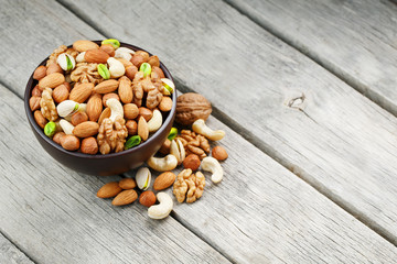 Wooden bowl with mixed nuts on a wooden gray background. Walnut, pistachios, almonds, hazelnuts and cashews, walnut.
