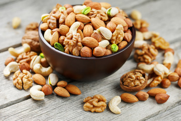 Wooden bowl with mixed nuts on a wooden gray background. Walnut, pistachios, almonds, hazelnuts and cashews, walnut.