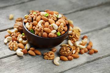 Wooden bowl with mixed nuts on a wooden gray background. Walnut, pistachios, almonds, hazelnuts and cashews, walnut.