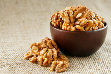 Peeled walnuts in a wooden, dark brown cup on a burlap cloth.