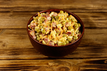 Mayonnaise salad with sausage, green pea, carrot and onion on wooden table