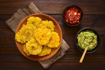 Patacon or toston, fried and flattened pieces of green plantains, traditional snack or accompaniment in the Caribbean, guacamole and tomato onion salad on the side