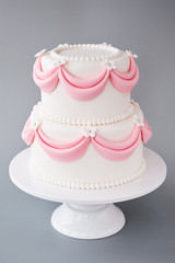 White wedding cake with pink elements made from pastry mastic on a gray background. Sugar flowers, marzipan flowers and mastic, beautiful decor for decorating cakes.