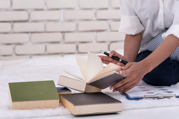 Woman sit on bed in room at home,read book and search information from book and laptop.