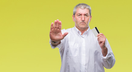 Handsome senior man holding credit card over isolated background with open hand doing stop sign with serious and confident expression, defense gesture